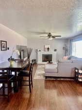 Dining area with a textured ceiling, wood-type flooring, a fireplace, and ceiling fan