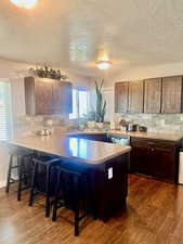 Kitchen featuring backsplash, a kitchen bar, dark wood-type flooring, and kitchen peninsula