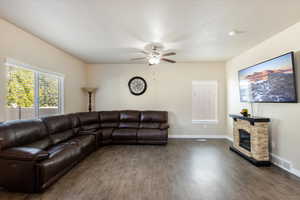 Living room with a textured ceiling, ceiling fan, dark wood-type flooring, and a stone fireplace