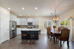 Kitchen with hanging light fixtures, a kitchen island with sink, stainless steel appliances, a notable chandelier, and dark hardwood / wood-style flooring