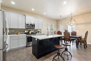 Kitchen featuring hanging light fixtures, an island with sink, white cabinets, stainless steel appliances, and a chandelier