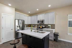 Kitchen featuring a center island with sink, white cabinetry, stainless steel appliances, dark hardwood / wood-style floors, and a kitchen bar