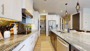 Kitchen with light stone counters, sink, white cabinetry, stainless steel appliances, and decorative light fixtures