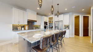 Kitchen with white cabinets, a center island with sink, stainless steel appliances, and light stone countertops