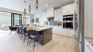 Kitchen featuring light stone counters, white cabinets, a center island with sink, and sink