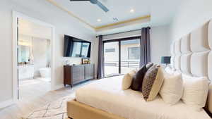 Bedroom featuring light wood-type flooring, a raised ceiling, connected bathroom, and ceiling fan