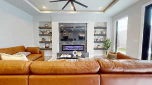 Living room featuring built in shelves, a high end fireplace, ceiling fan, and a raised ceiling