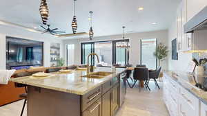 Kitchen featuring pendant lighting, white cabinetry, light stone counters, and sink