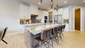 Kitchen with light stone counters, a kitchen island with sink, white cabinets, light hardwood / wood-style flooring, and stainless steel appliances