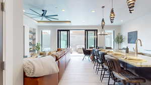 Living room with built in shelves, sink, light hardwood / wood-style flooring, a tray ceiling, and ceiling fan with notable chandelier