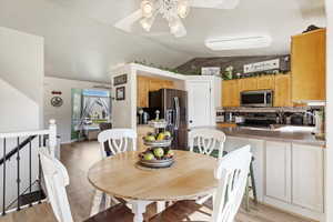 Dining area featuring ceiling fan, sink, light wood-type flooring, and vaulted ceiling