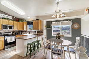 Kitchen featuring ceiling fan, backsplash, appliances with stainless steel finishes, a breakfast bar, and light wood-type flooring