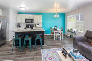 Kitchen featuring wood-type flooring, tasteful backsplash, white cabinetry, black appliances, and decorative light fixtures