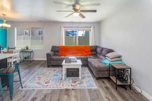 Living room with ceiling fan with notable chandelier and light wood-type flooring