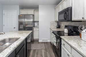 Kitchen with light stone counters, sink, tasteful backsplash, black appliances, and dark hardwood / wood-style flooring