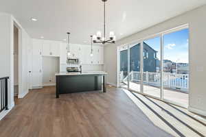 Kitchen with hanging light fixtures, white cabinetry, hardwood / wood-style floors, an island with sink, and stainless steel appliances