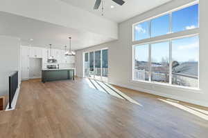 Unfurnished living room with sink, light wood-type flooring, ceiling fan with notable chandelier, and a wealth of natural light