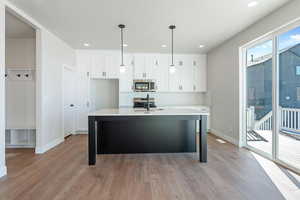 Kitchen featuring decorative light fixtures, white cabinetry, appliances with stainless steel finishes, and a kitchen island with sink