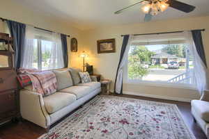 Living room with ceiling fan, dark wood-type flooring, and a wealth of natural light