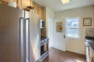 Kitchen featuring dark stone countertops, backsplash, premium appliances, light brown cabinetry, and dark hardwood / wood-style floors