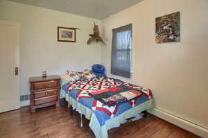 Bedroom with baseboard heating and dark hardwood / wood-style flooring