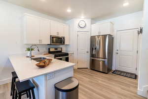 Kitchen with appliances with stainless steel finishes, light hardwood / wood-style floors, white cabinets, a kitchen bar, and sink