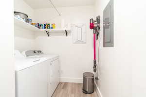 Washroom with light wood-type flooring, electric panel, and washer and clothes dryer