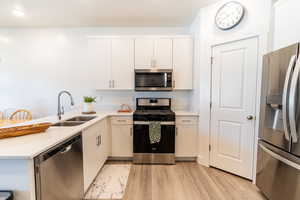 Kitchen with white cabinetry, kitchen peninsula, stainless steel appliances, light wood-type flooring, and sink