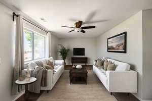 Carpeted living room with a textured ceiling and ceiling fan, this room is virtually staged in this photo.