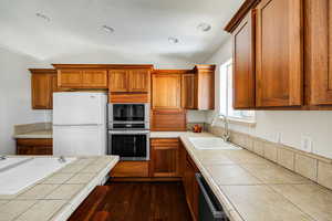 Kitchen featuring white refrigerator, tile countertops, sink, and stainless steel oven