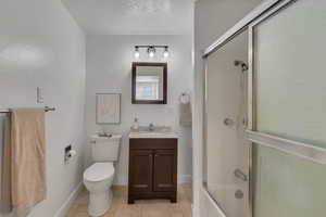 Full bathroom with vanity, toilet, combined bath / shower with glass door, and tile flooring