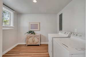 Laundry Room featuring washer and dryer, electric panel, and light hardwood flooring.