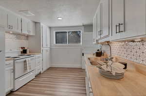 Kitchen with tasteful backsplash, white cabinets, white appliances and door to upstairs mother-in-law.