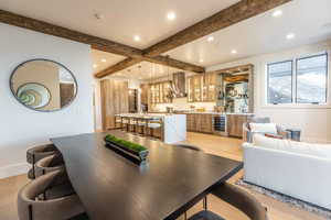 Dining area with beam ceiling, wine cooler, light hardwood / wood-style flooring, and indoor wet bar