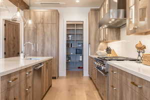 Kitchen with hanging light fixtures, sink, light hardwood / wood-style flooring, wall chimney range hood, and appliances with stainless steel finishes