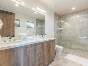 Bathroom featuring a tile shower, vanity, and toilet