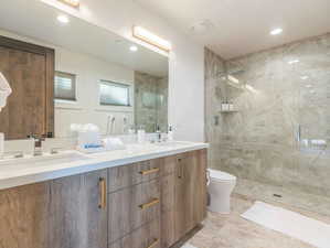 Bathroom featuring a tile shower, vanity, and toilet