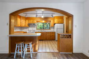 Kitchen featuring rail lighting, white appliances, kitchen peninsula, light wood-type flooring, and sink