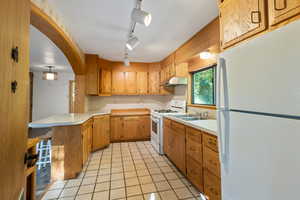 Kitchen featuring light tile patterned flooring, sink, kitchen peninsula, rail lighting, and white appliances