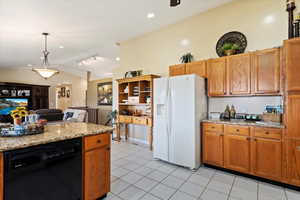 Kitchen with light stone counters, white refrigerator with ice dispenser, dishwasher, and lofted ceiling