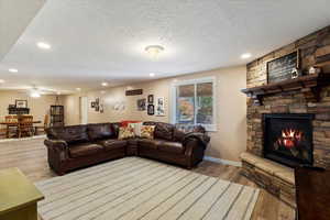 Living room featuring ceiling fan, light hardwood / wood-style floors, a fireplace, and a textured ceiling