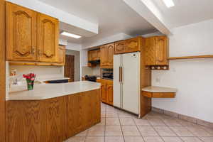 Kitchen featuring light tile patterned floors, sink, kitchen peninsula, extractor fan, and white fridge