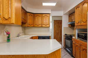 Kitchen featuring light tile patterned flooring, sink, kitchen peninsula, and black appliances