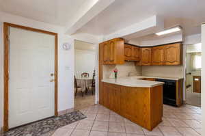 Kitchen with light tile patterned floors, black dishwasher, sink, and kitchen peninsula