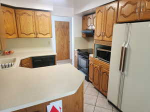 Kitchen featuring kitchen peninsula, light tile patterned floors, exhaust hood, black appliances, and sink