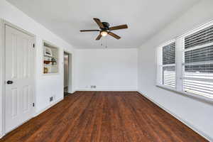 Unfurnished room featuring ceiling fan, built in features, and dark wood-type flooring