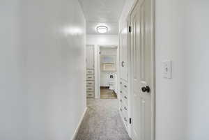 Hallway with light carpet and a textured ceiling