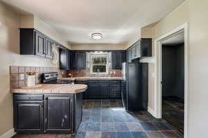 Kitchen featuring black fridge, sink, tasteful backsplash, tile counters, and stainless steel range with electric cooktop