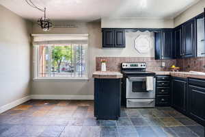 Kitchen with tile counters, decorative backsplash, stainless steel electric range, and decorative light fixtures