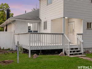 Back house at dusk featuring a wooden deck and a yard